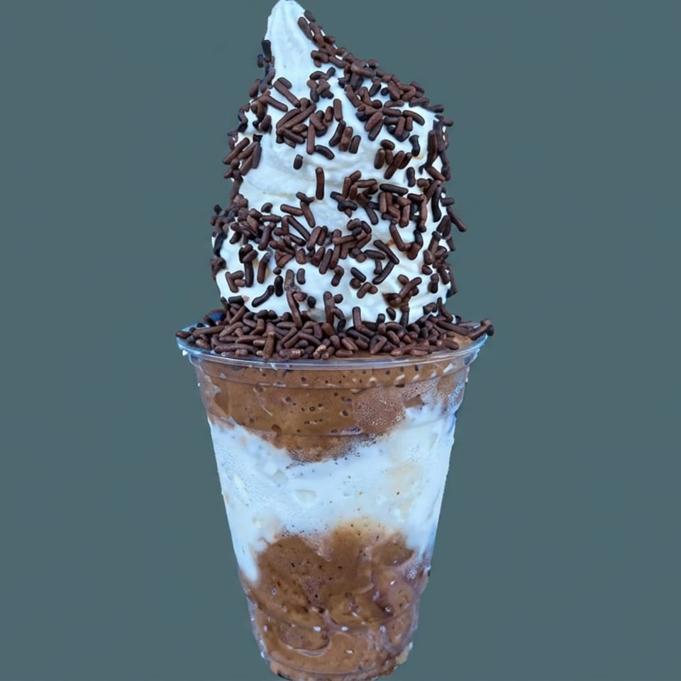 Layered chocolate and vanilla dessert in a clear cup, topped with whipped cream and chocolate sprinkles.